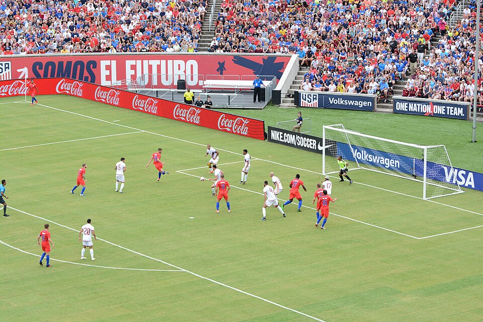 Jugador ejecutando un saque de esquina en un partido nocturno